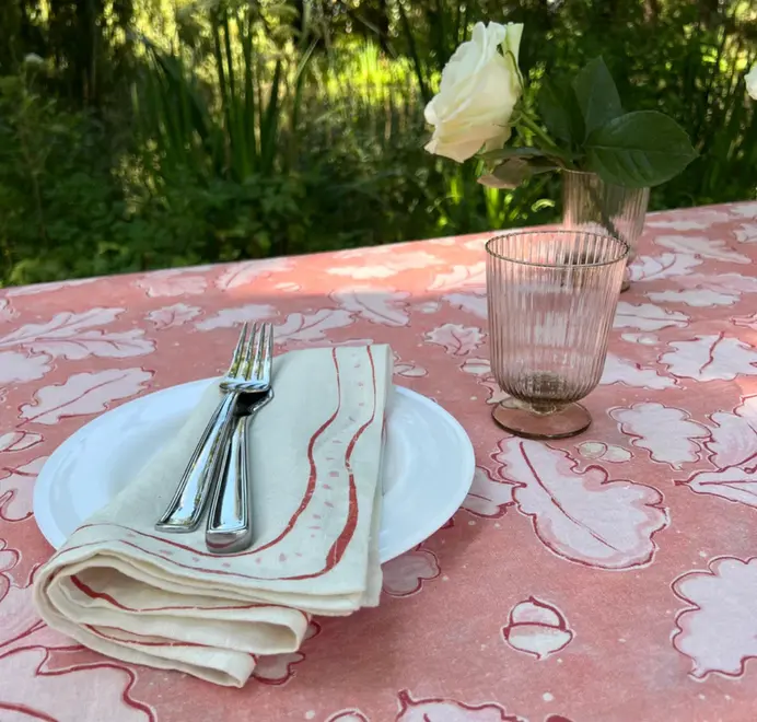 Grace Oak Trees Pink Linen Tablecloth. Light Pink and white tablecloth with oak patterns, styled on an outdoor dining table with plates, glassware, and white floral arrangements.
