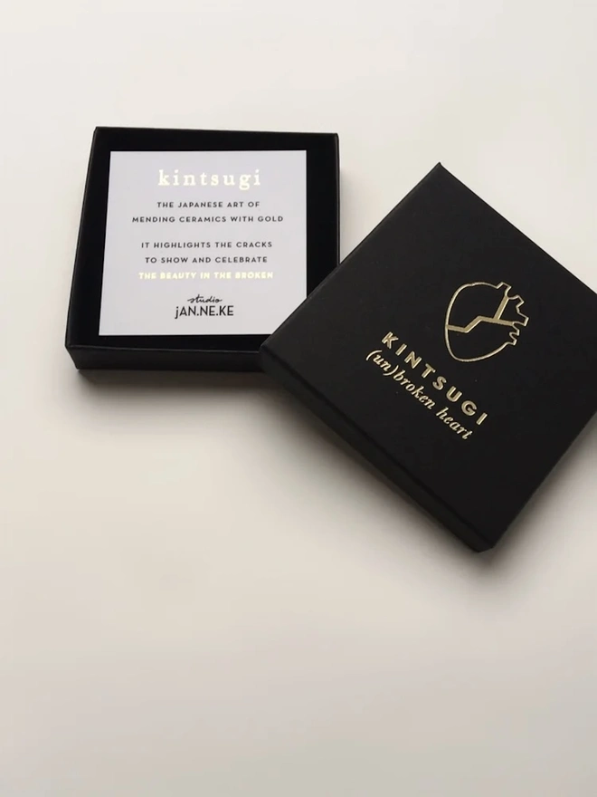(Un)Broken Heart Pin, a black box with a card explaining the white and gold heart pin. 