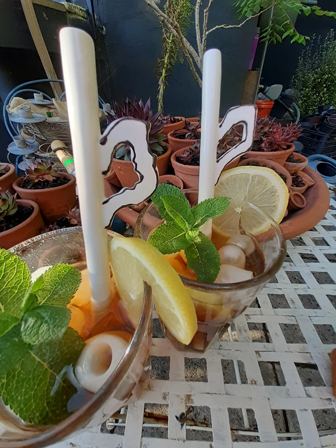 Handmade ceramic iced tea straws displayed in tall glasses with lemon slices, mint, and ice outdoors