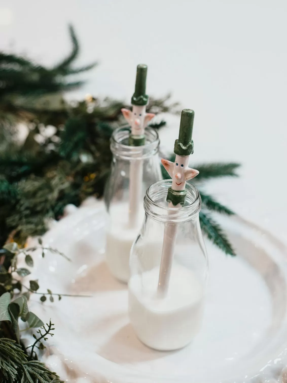 Bill and Ben Ceramic Elf straws seen in a jar of milk on a white plate surrounded by Christmas greenery