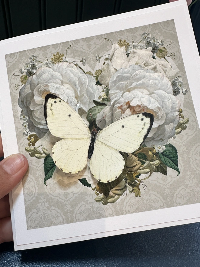 A handmade Wedding Anniversary Card, showing a vintage, floral heart with white roses and a 3D papercut butterfly, whose wings are pulled out to give an extra dimension to the card.