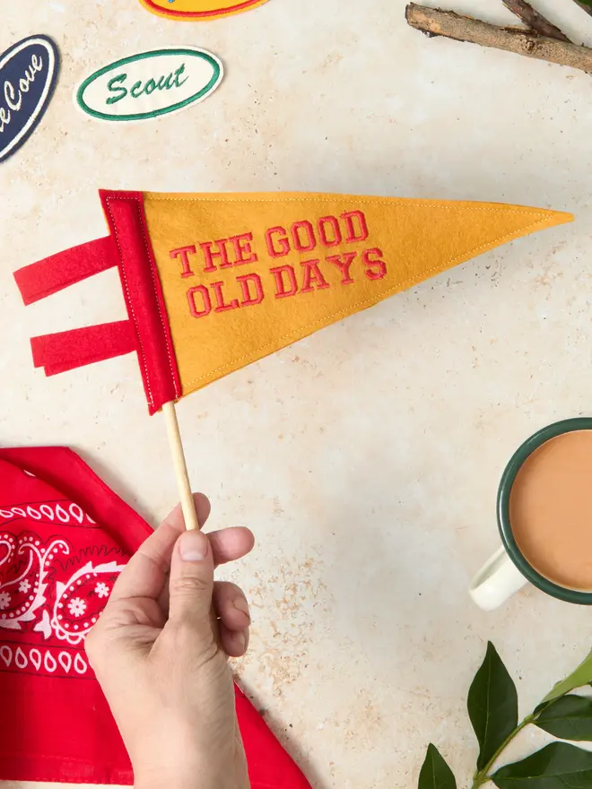 A red and yellow The good old days mini pennant flag on a wooden pole being held in a hand
