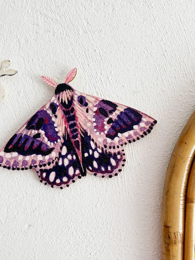 wooden moth wall decoration. purple wooden moth hung on plain white wall.