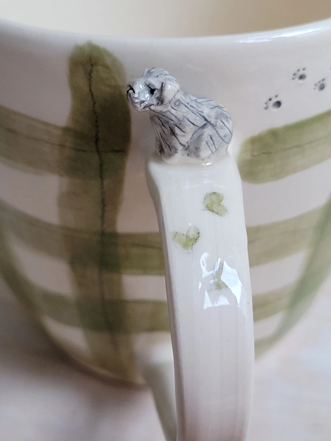 close up of a ceramic green check mug with a miniature schnauzer figure on the handle and hand painted pawprints and hearts 