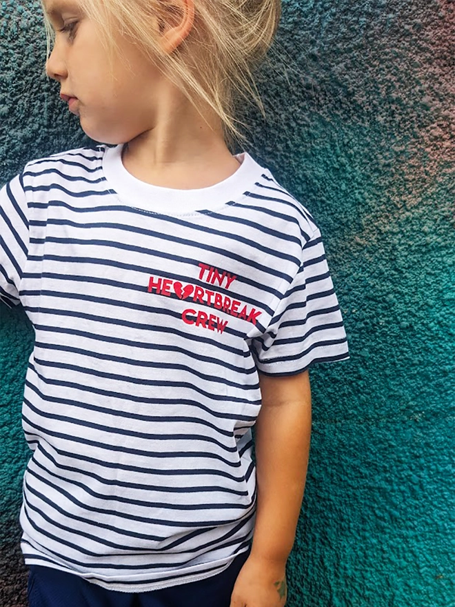 Child wearing a navy and white stripe t-shirt with red Tiny Heartbreak Crew slogan.