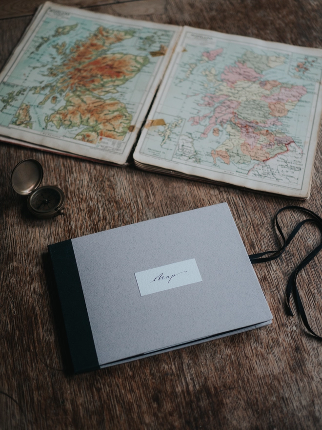 Handbound map with a pink cover and calligraphy label on a table with a compass and vintage atlas