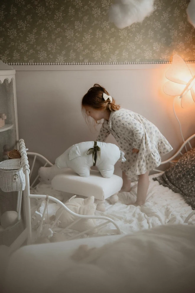 Cotton Pig Plushie, a child with their pig plushie sitting on their bed. 