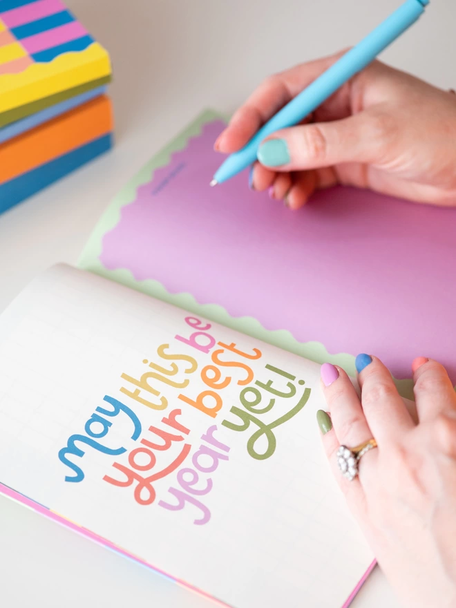 Inside the Raspberry Blossom weekly planner, colourful rainbow hand lettered positive message reads 'May this be your best year yet'