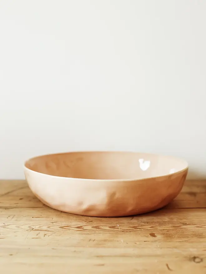 'sunrise' handcrafted stoneware bowls. a large pink bowl on a wooden bench.