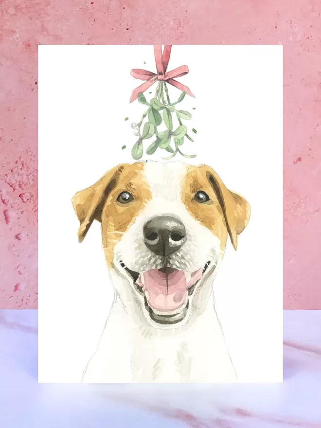 A Christmas card featuring a hand painted design of a Jack Russell Terrier, stood upright on a marble surface.