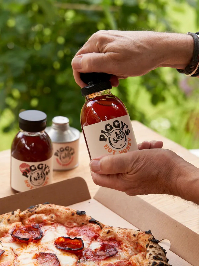 Piggy's Hot Honey- held up against a pizza in the garden 