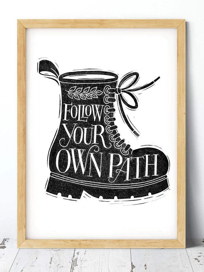 white hand lettering inside chunky black boot in a wooden frame