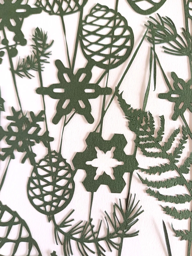 Closeup of detail of winter, dark green initial papercut including pinecones, snowflakes, ferns, and spruce