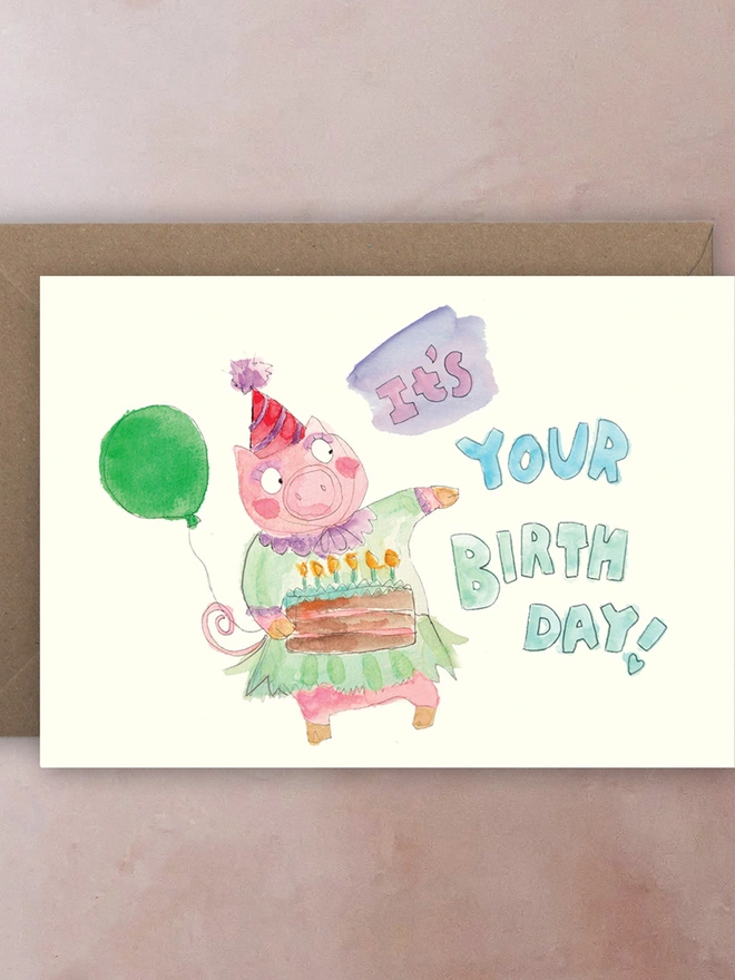 A pig with a party hat, birthday cake and balloon with "it's your birthday" text.