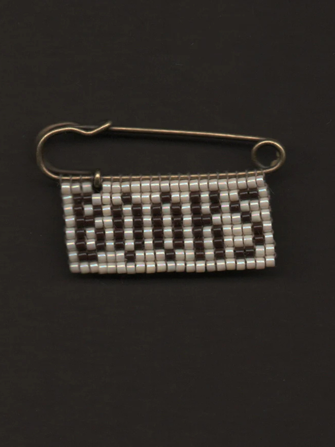 'lingua v' beaded 'books' pin. a beaded pin badge with 'books' in brown letters on a pearl background.