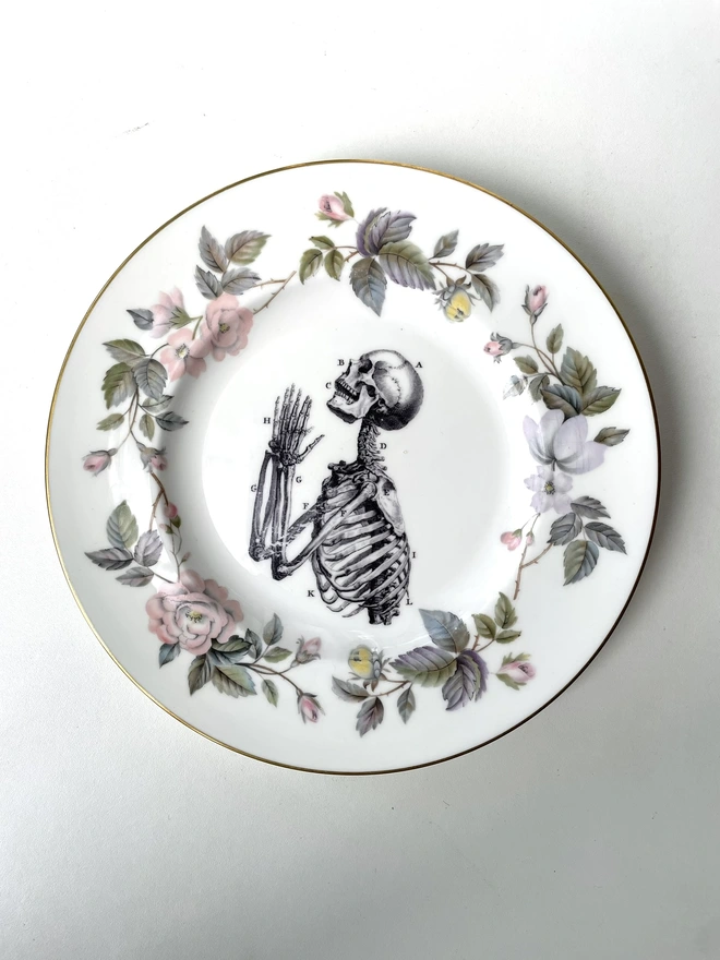 vintage plate with an ornate border, with a printed vintage illustration of a praying skeleton in the middle