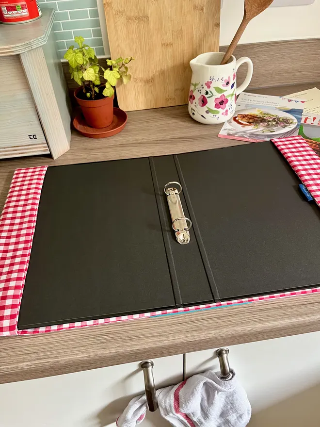 Red Gingham Covered Ring Binder open on a wooden kitchen bench, showing 2 metal rings