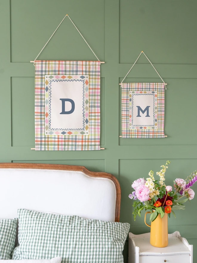 Personalised Gingham Initial Fabric Banner, in rainbow hanging on a green wall. 