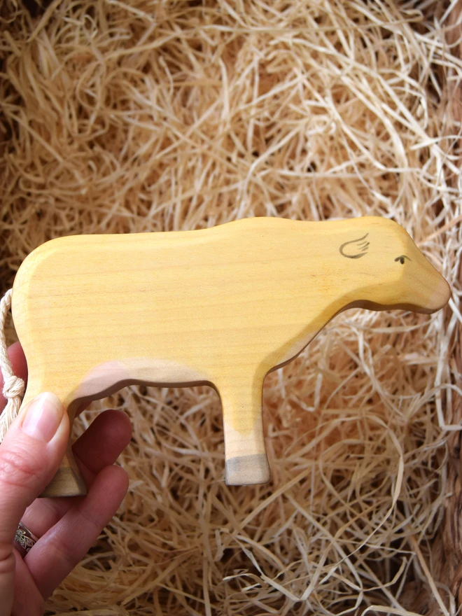 wooden toy cow being hel din hand above woodwool