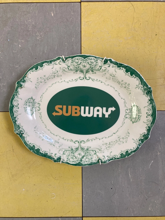 Vintage decorative white and green china plate featuring a Subway logo