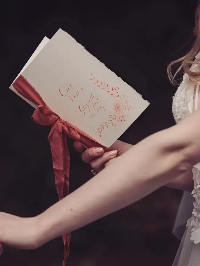 personalised calligraphy wedding vow booklet. white booklet with rust red calligraphy on cover.