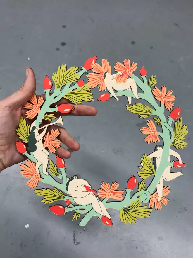 Fiona holds a finished colourful woodland wreath, made of leaves, rosehips and 4 nudie nymphs