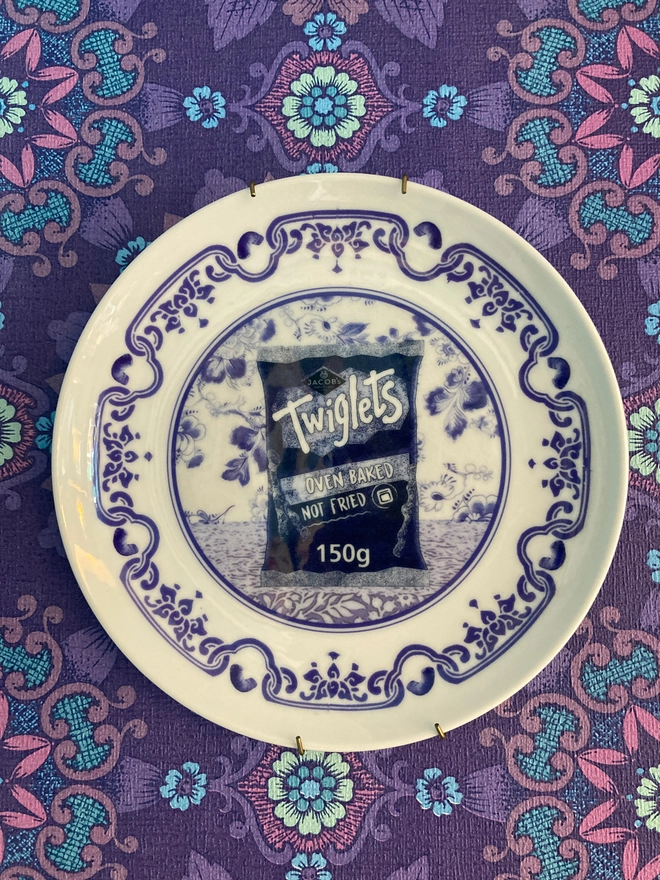 An 8" blue and white 'Delft' style plate featuring a packet of Twiglets