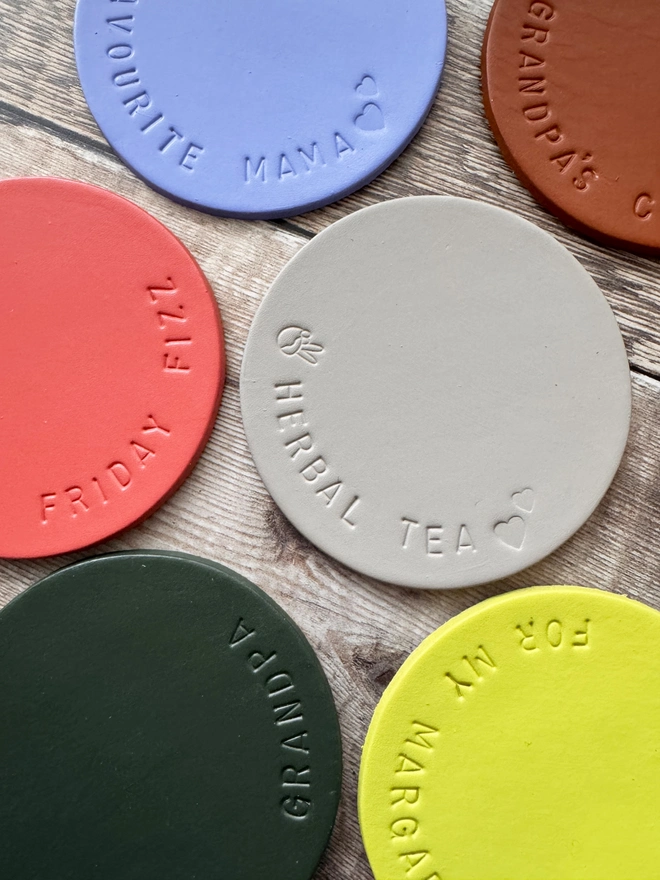 Handmade leather coasters in various colours, embossed with personalised messages like 'Herbal Tea' and 'Favourite Mama.' Stylish and durable drink coasters, perfect for gifts and home decor.