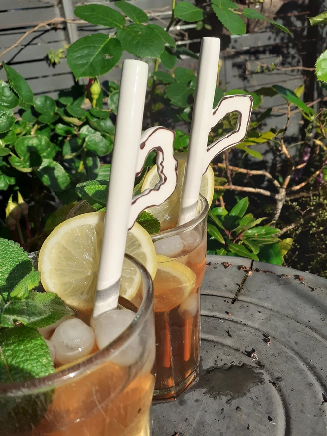 Pair of quirky ceramic drinking straws with tiny teacup handles in refreshing summer beverages