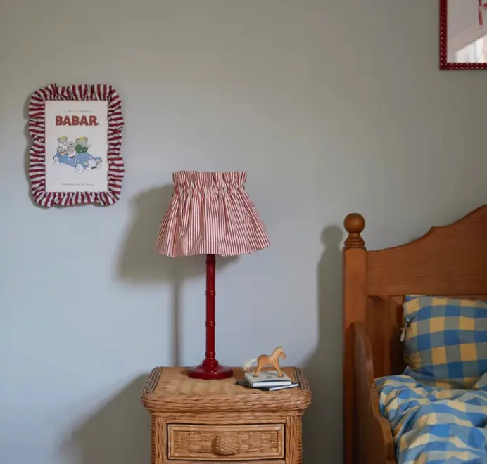Soft ruffle frame with red and white striped fabric trim displaying a Babar print hanging on the wall in a kids bedroom.