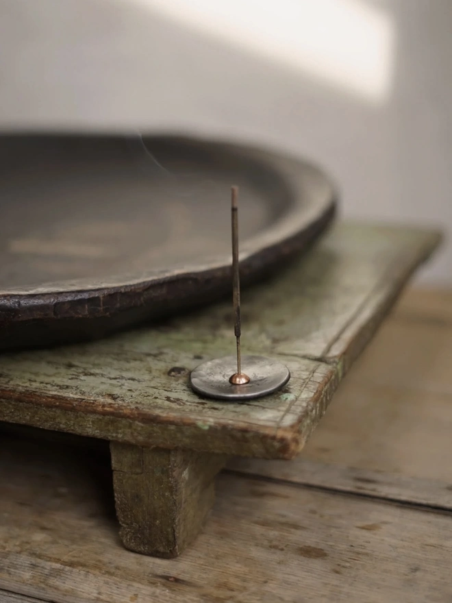 Copper And Steel Incense Holder, a metal incense holder sitting on a wooden surface in a workshop. 