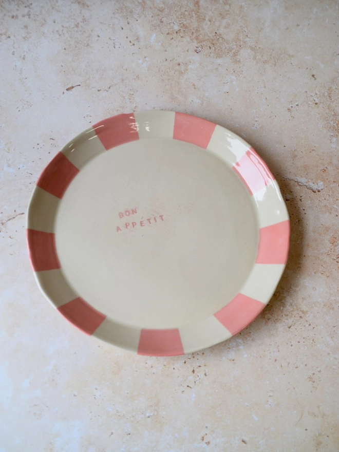 Handmade ceramic plate with pink and cream striped rim — “Bon Appétit” text in centre