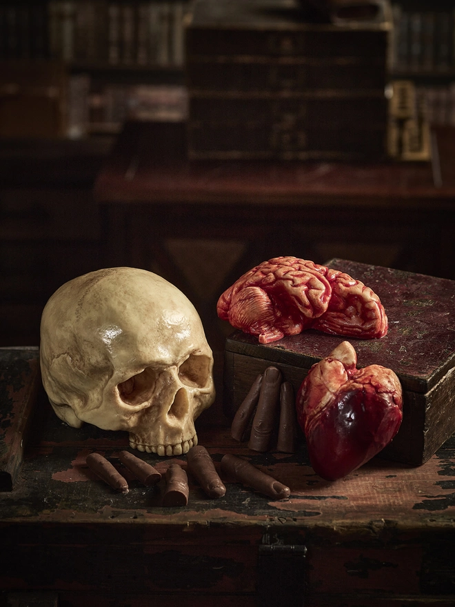 Realistic edible chocolate human brain arranged on antique table with chocolate human skull, heart and fingers