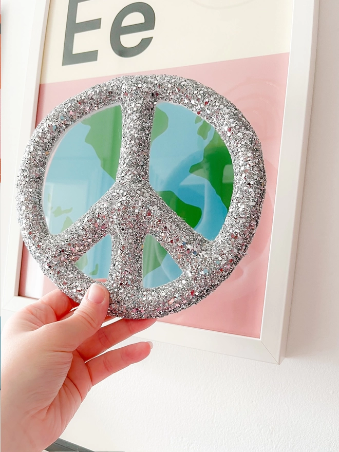 Silver glitter peace sign being held up in front of a picture of the earth