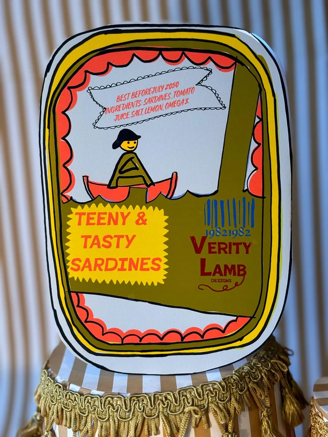 Leda Tin Card, a colourful card sitting on a decorated display in front of a backdrop. 