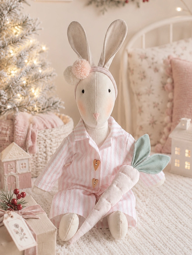 Christmas Eve Veronica Bunny in pink striped pyjamas holding a handmade carrot for Santa’s reindeer in a softly styled festive nursery.