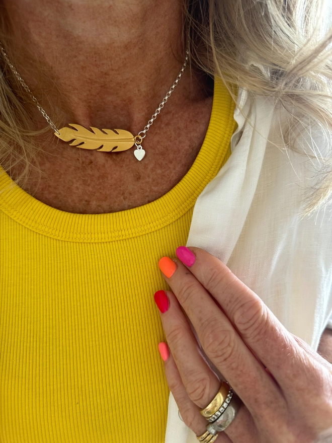 model wears a gold plate feather charm on a sterling silver chain with additional silver mini heart