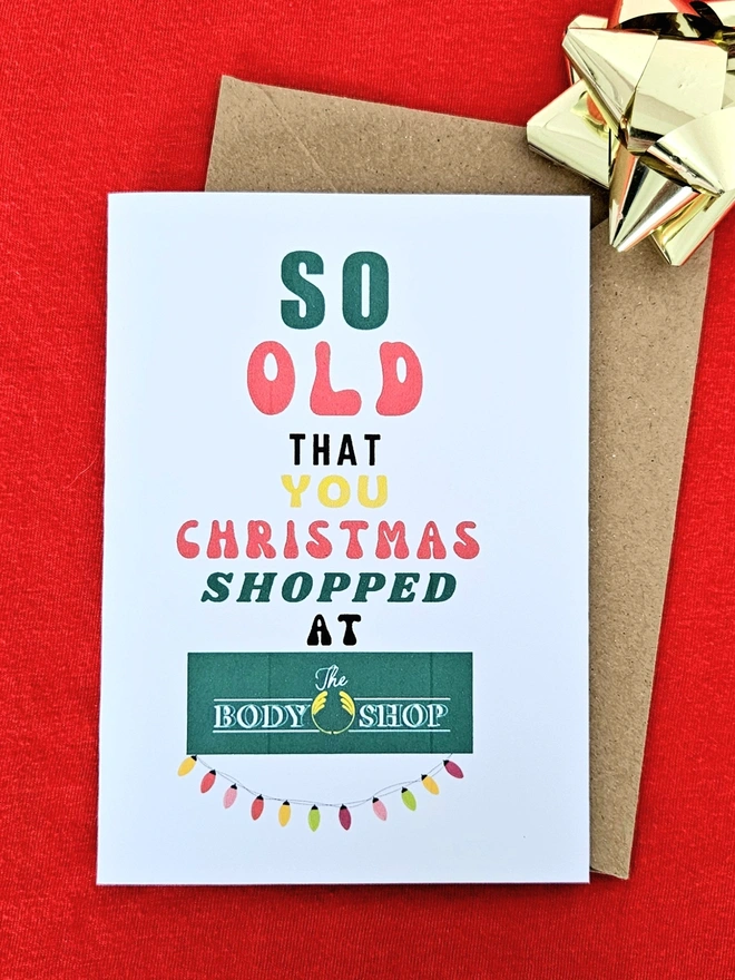A photograph of the front of a humorous A6 greeting card illustrated using brightly coloured text and the retro shop logo. The text says so old you Christmas shopped at Body Shop with an illustration of vintage string fairy lights.
