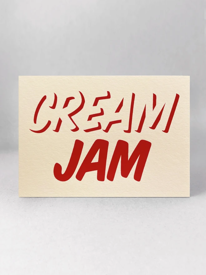 Jam on the bottom, Cream on top, printed in red ink on this cream card. Stood in a light grey studio with soft shadows.