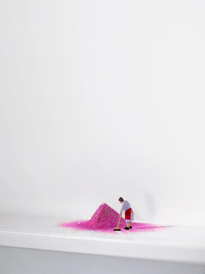 Miniature scene in an artbox showing a tiny cleaning lady sweeping up a huge pile of pink glitter 