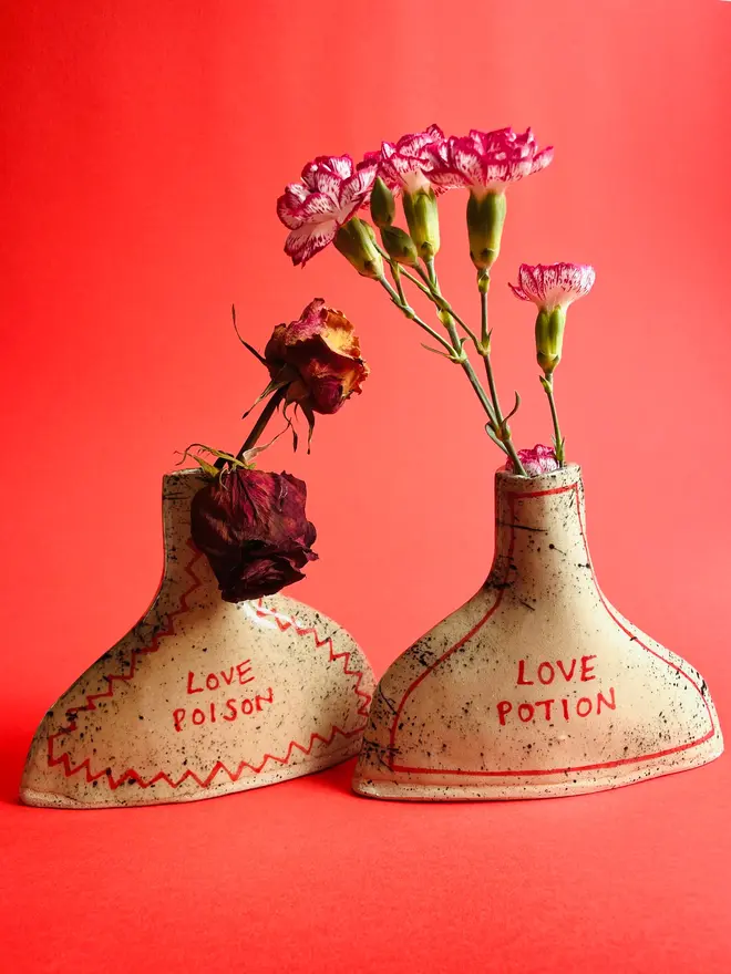 Love Potion/ Poison Bottle Vase, a pair of ceramic vases that either say 'love poison/ love potion'. Each is stamped with a signature red dot on the bottom. 