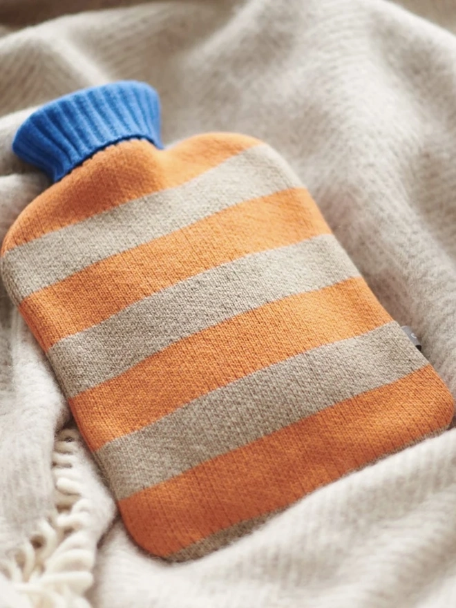 Lambswool Hot Water Bottle Cover, a colourful hot water bottle cover sitting on a blanket. 