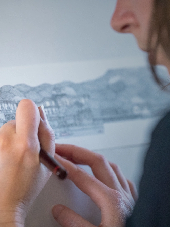 Artist Katherine Jones using a pen to hand-draw Bristol harbour with boats and surrounding buildings 