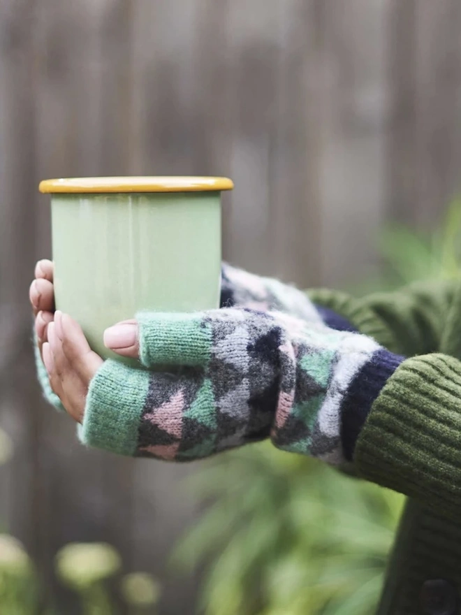 Women's Grey & Mint Triangle Lambswool Wrist Warmers, a woman wearing a pair of colourful wrist warmers outside. 