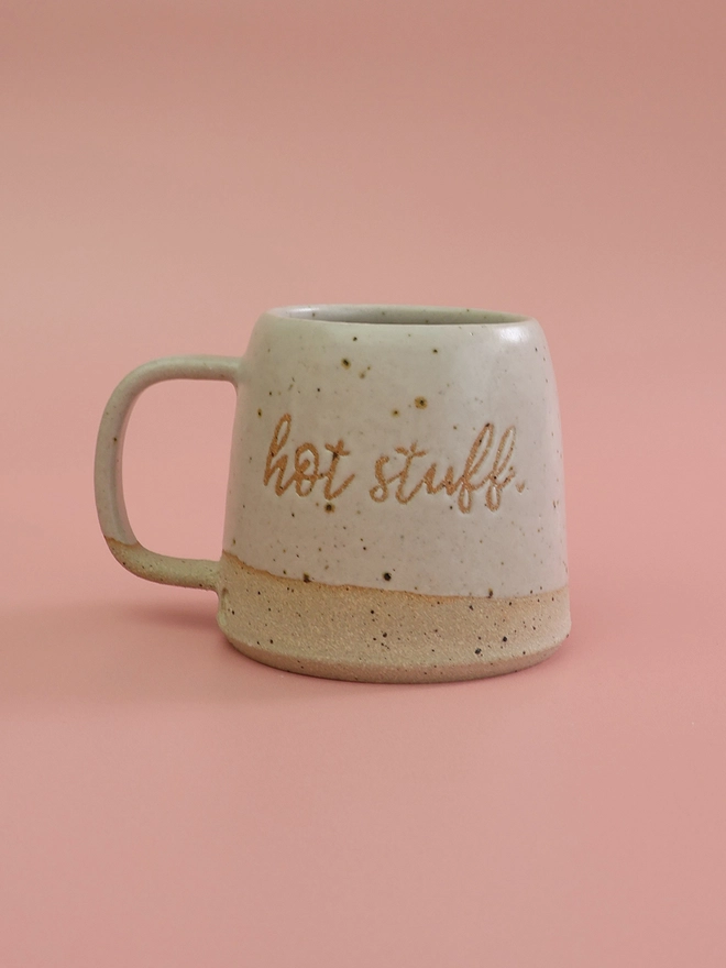hot stuff text in a flowing script style on a handmade white stoneware mug which is on a pink background