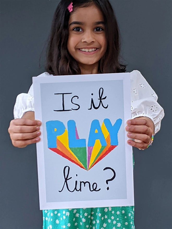 Young girl standing holding an art print saying 'Is it play time?'
