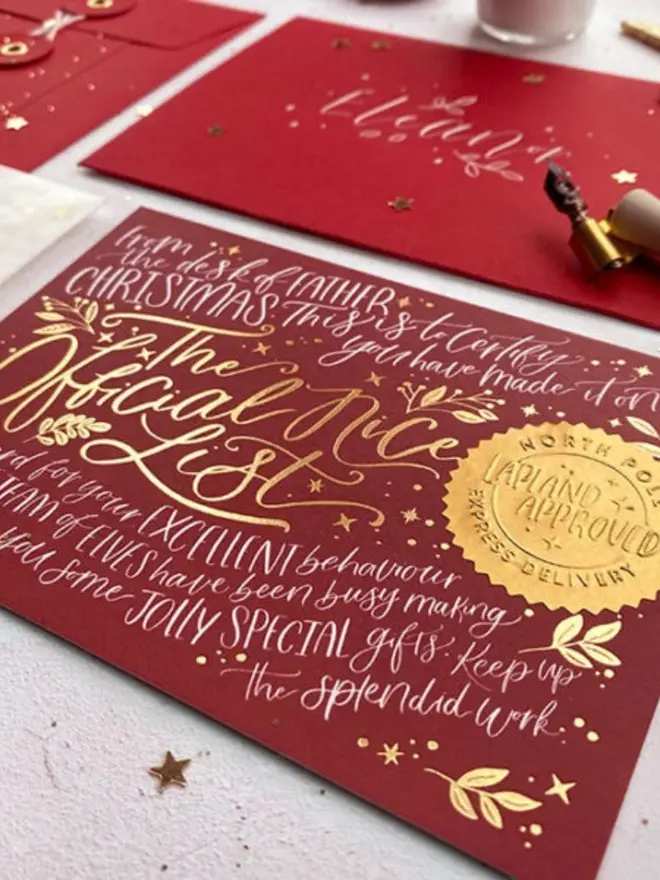 Close-up of a gold foil "The Official Nice List" certificate and embossed "Lapland Approved" seal on deep red card.