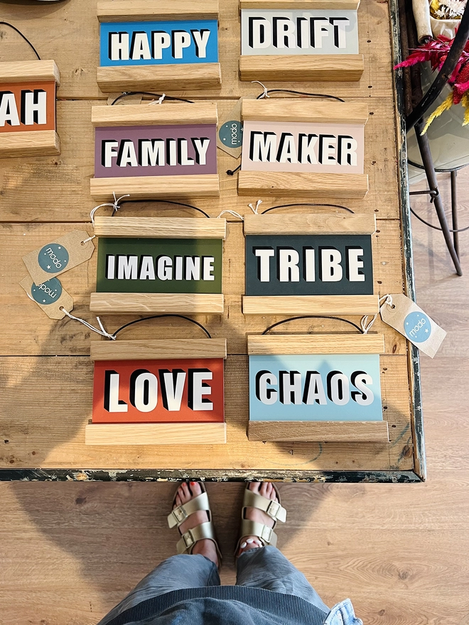 A wide shot of colour prints framed in oak hangers, reading HAPPY, DRIFT, FAMILY, MAKER, IMAGINE, TRIBE, LOVE & CHAOS 
