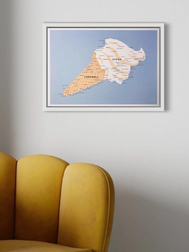 A framed print of an ice cream that also looks like a map of Devon and Cornwall is hung on a white wall above a yellow velvet scalloped chair.