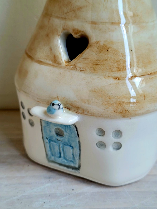 close up of a ceramic house shaped vase with a blue door and blue tit bird above the door with a cut out heart in the roof